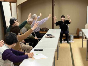 講師と参加者が腕を上げ、指の動きを使った課題に挑戦している様子。