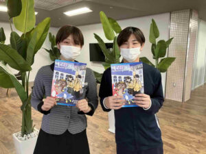 鳳凰高等学校フリーマガジン「Mマガ」を手にするニコニコタウンきいれのスタッフ