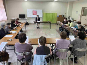 鹿児島市谷山福祉館で在宅サービスについて説明する講師と資料を確認する参加者の様子