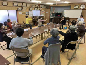 森山公民館の福笑会サロンで、参加者が円になり手足を動かしながらコグニサイズに取り組んでいる様子