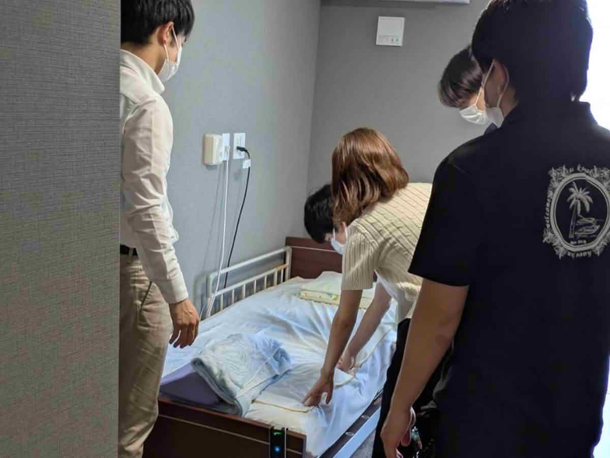 うすきの里の居室で、ベッドに設置された介護機器を見学する鹿児島国際大学 中井ゼミの学生
