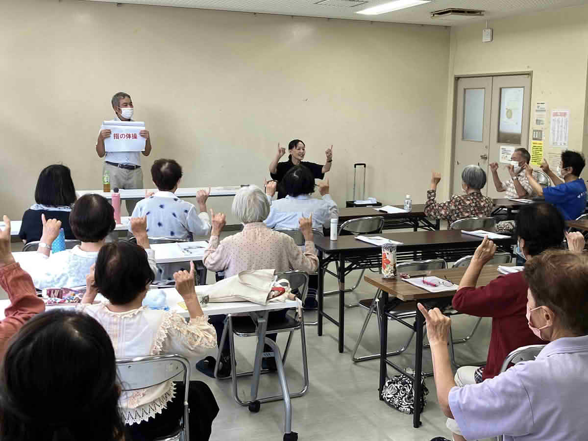 西谷山福祉館で参加者が講師の動きに合わせて指の体操に取り組む様子