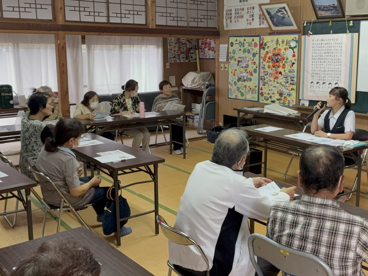 一番組公民館で、講師がマイクを持って説明し、参加者が資料を見ながら話を聞いています。