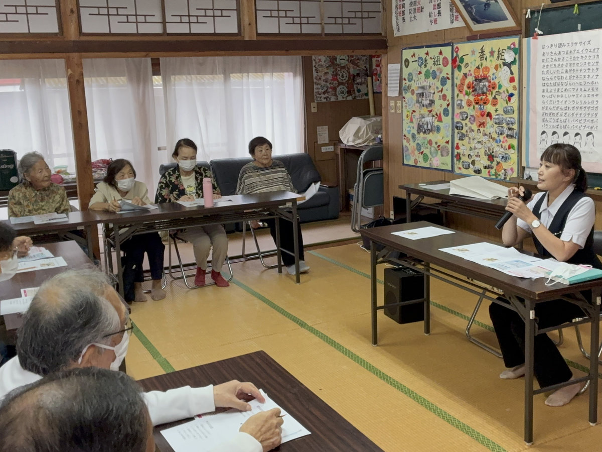 一番組公民館で、講師の説明に参加者が耳を傾けています。机の上には配布資料が置かれています。