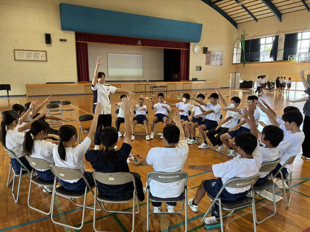 指宿市立南指宿中学校の福祉体験学習で、椅子に座った生徒たちが両手を上げてコグニサイズに取り組む様子