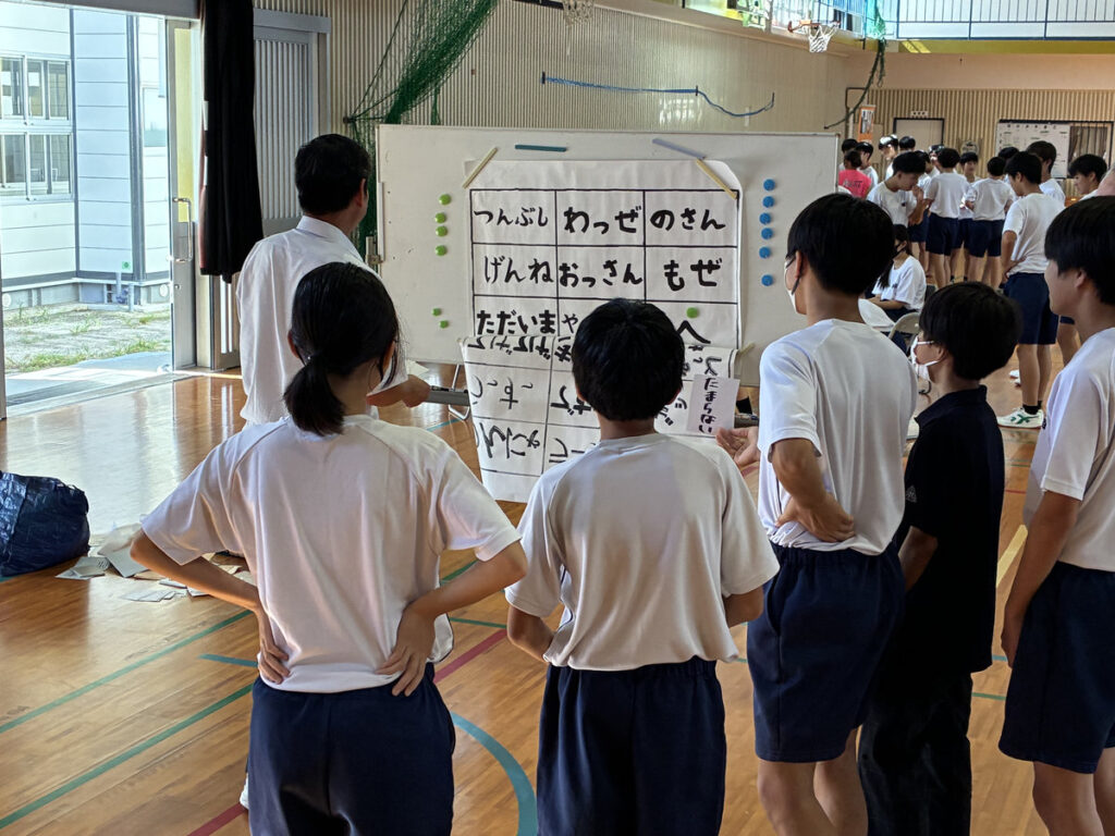 南指宿中学校の福祉体験学習で、掲示された説明資料を囲みながら、スタッフの説明を聞く生徒たちの様子