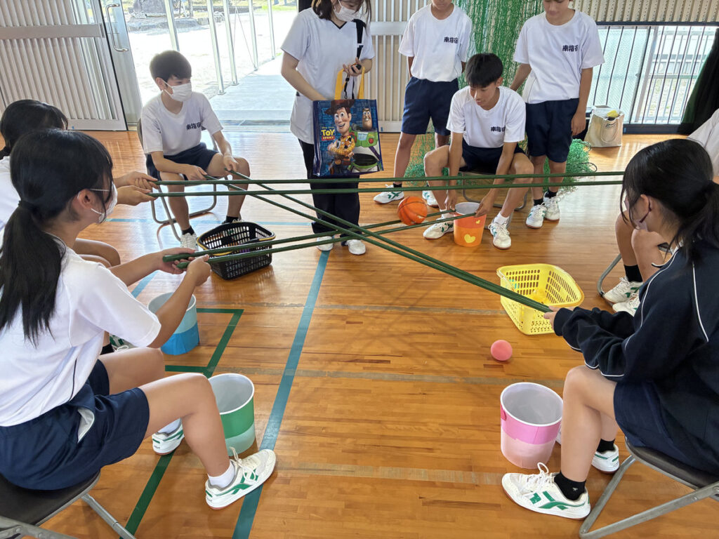 南指宿中学校の生徒たちが、テーブル上に設置された用具やカラフルなボールを使ったゲーム式レクリエーションに取り組む様子