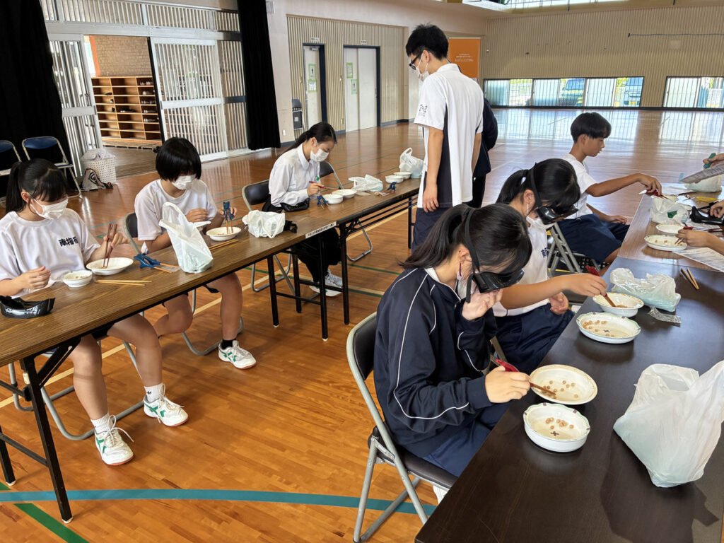 南指宿中学校の福祉体験学習で、生徒たちがテーブルを囲み、スタッフの見守りのもと体験活動に取り組んでいる様子