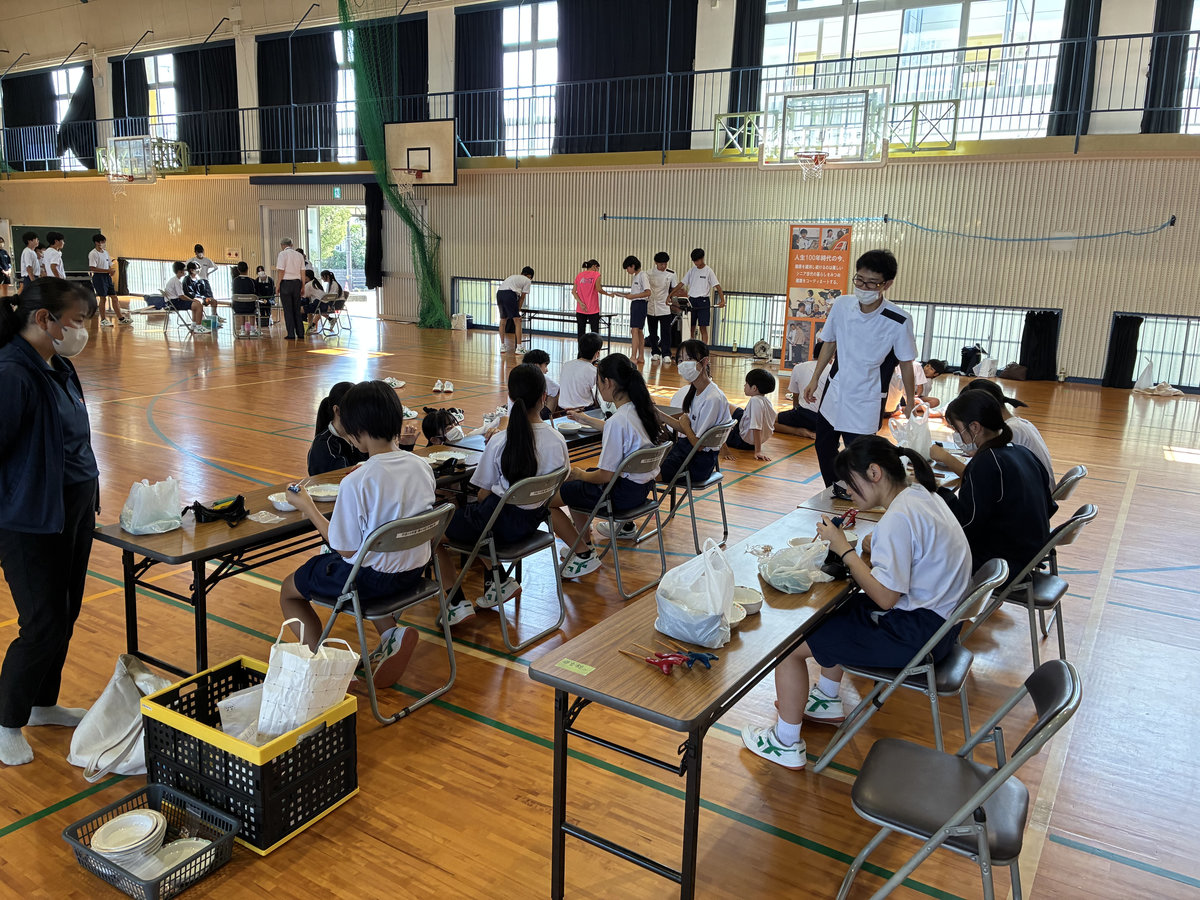 南指宿中学校の体育館に設けられた体験ブースで、生徒たちがグループに分かれて福祉体験学習に参加している様子